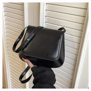 Detail of black leather crossbody bag with adjustable strap and golden buckle buckle