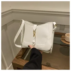 Detail of white leather shoulder bag with gold metal buckle held by model in cafe setting