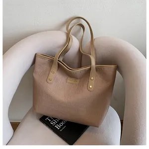 Detail of embossed apricot tote bag with gold metal logo on a modern chair