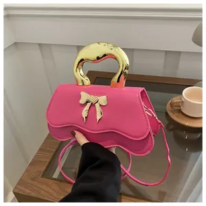 Detailed view of pink crossbody bag with gold bow clasp and metallic handle on table