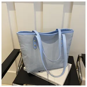 Detail of light blue tote bag with pleated texture and golden rivet strap accents