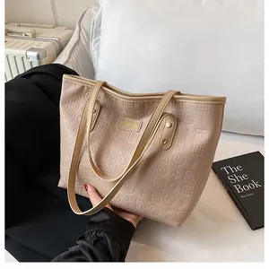 Close-up of beige tote bag featuring embossed letter patterns and golden fashion metal tag
