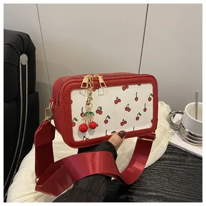 Close-up of cherry print crossbody bag featuring wide red strap and metal charm detail