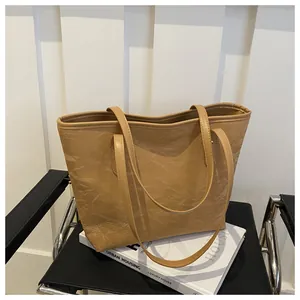 Detailed view of large tan tote bag with unique crinkled texture on a black leather chair