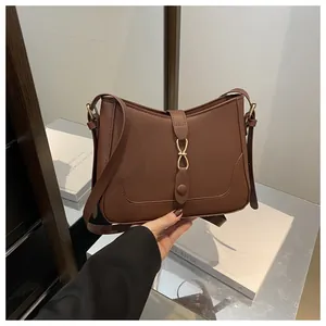 Detail of a brown matte leather shoulder bag featuring a unique gold interlocking buckle