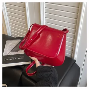 Close-up of red patent leather shoulder bag with glossy finish and gold metal buckle