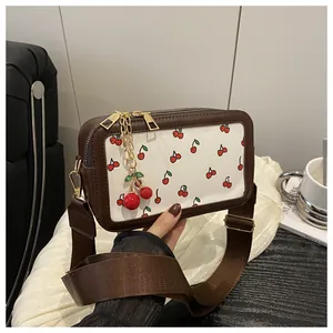 Detail of square crossbody bag featuring cherry print and golden hardware with a wide strap