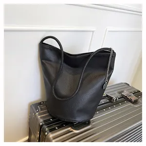Detail of black lychee grain leather bucket bag with silver chain on silver suitcase