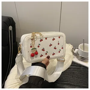 Close-up of white crossbody bag featuring cherry print, gold zipper, and cherry charm