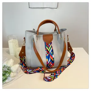 Dettaglio borsa in pelle PU bicolore con tracolla in tessuto colorato su tavolo