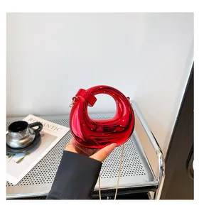 Macro detail of glossy red metallic handbag with sculpted ring handle and golden chain strap