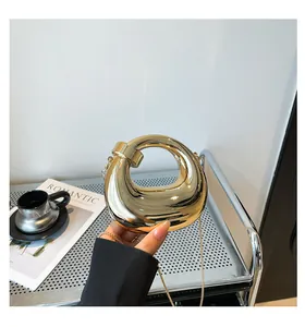 Detail of a round gold mirror clutch bag with metallic chain and donut-shaped hollow design