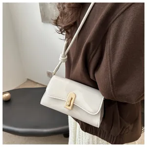 Close-up of white patent leather shoulder bag with golden clasp worn by a model