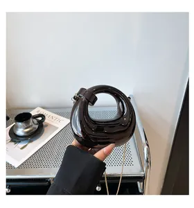 Close-up of black glossy acrylic ring handbag with gold chain held by a hand