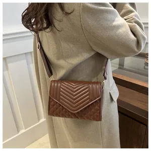 Detail van de donkerbruine gewatteerde crossbodytas met chevron-stiksel en gouden gespen