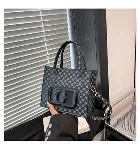 Close-up of small printed tote bag with G-letter logo, gold hardware, and long shoulder strap