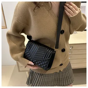 Detail van zwarte crossbodytas met V-vormige en ruitvormige stiksels en gouden accenten