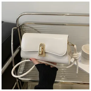 Detail of white faux leather shoulder bag featuring a gold arch lock and knotted strap