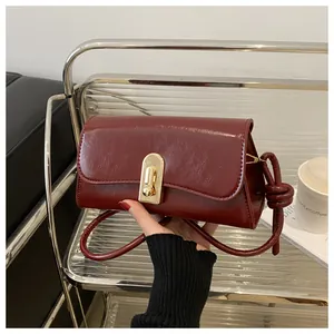 Detail of burgundy glossy oil wax leather handbag with golden twist lock and knot strap