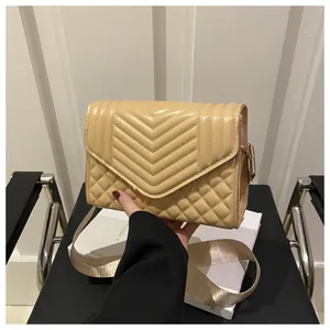 Detail van beige gewatteerde crossbodytas met V-patronen en gouden brede schouderband