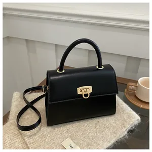 Detail einer schwarzen matten Ledertasche mit goldenem Drehverschluss auf Holz