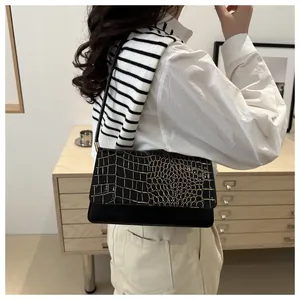 Detail of trendy black faux crocodile skin shoulder bag worn by model in cozy interior