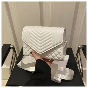 Detail van witte gewatteerde crossbodytas met chevronstiksel en een brede stoffen riem