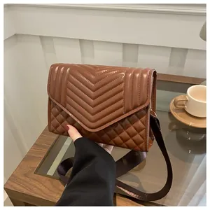 Detail van bruine gewatteerde crossbodytas met brede stoffen riem en V-stikselstructuur