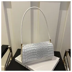 Detail view of white crocodile pattern leather shoulder bag on an elegant prop book