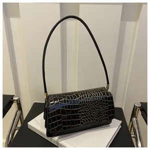 Close-up of black glossy patent leather shoulder bag with gold crocodile embossed texture