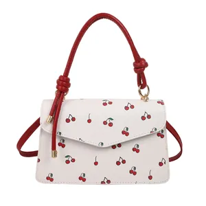 Stylish white crossbody handbag with red cherry pattern and red rope handle