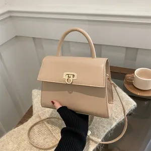 Elegante beige quadratische Handtasche mit Goldschloss, in der Hand vor warmem Grund