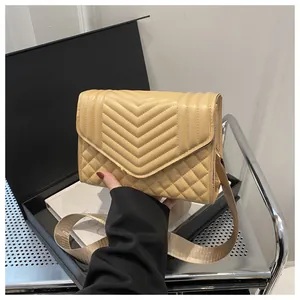 Detail van beige gewatteerde tas met v-stikselpatroon en brede geweven riem