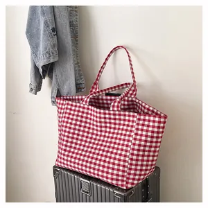 Détail d'un grand sac cabas à carreaux rouges posé sur une valise argentée de voyage