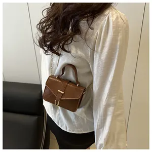 Detail view of brown leather crossbody bag with gold U-buckle worn by a model