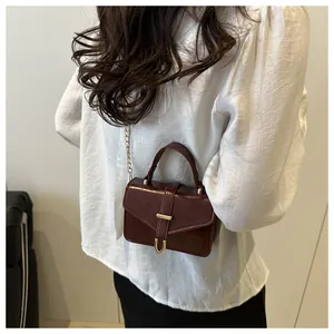 Detail of burgundy crossbody bag with gold metal handle and elegant chain strap on a model