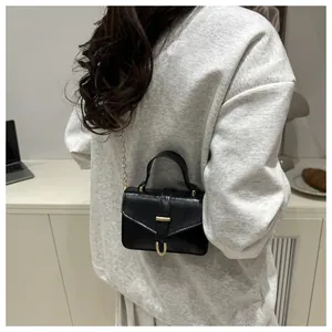 Close-up of black crossbody bag with gold metal buckle on a grey sweatshirt
