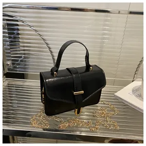 Detail of black crossbody bag showing golden chain strap and polished metal hardware