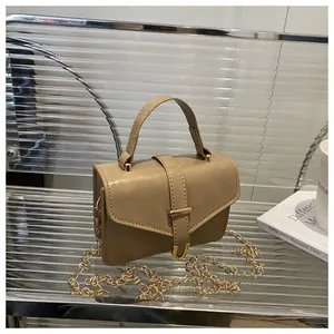 Detail of khaki PU leather bag with gold metal buckle and chain on glass shelf