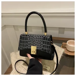 Detail einer schwarzen Handtasche mit Krokostruktur und Goldverschluss auf einem Pullover