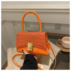 Detailansicht der orangefarbenen Handtasche mit Krokoprägung und goldenem Drehverschluss