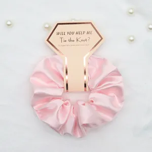 Dettaglio scrunchie in raso rosa con biglietto per damigella d'onore e decoro di perle
