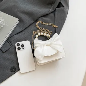 Detailed view of white mini crossbody bag with chiffon bow and pearl handle on grey blazer
