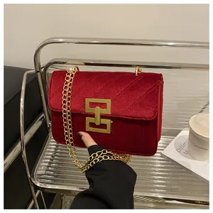Macro shot of burgundy velvet crossbody bag with quilted texture and golden chain strap