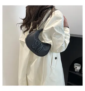 Model wearing a black crescent shoulder bag with embossed letters and gold hardware