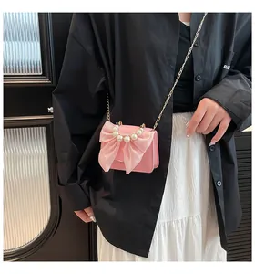 Pink mini crossbody bag featuring a large mesh bow and white pearl handle on a model
