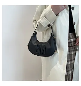 Detail of black leather croissant bag with embossed letters and golden buckle