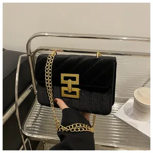 Detail of black velvet crossbody bag with gold chain strap and geometric metal buckle
