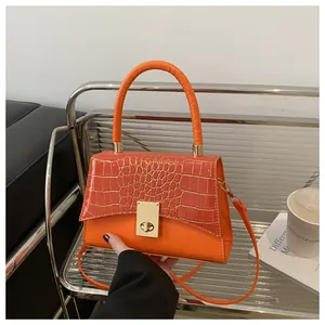 Detail der orangefarbenen Handtasche mit Krokodilprägung und goldenem Drehverschluss