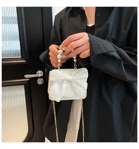 Close-up of white crossbody bag with organza bow, pearl handle, and gold chain